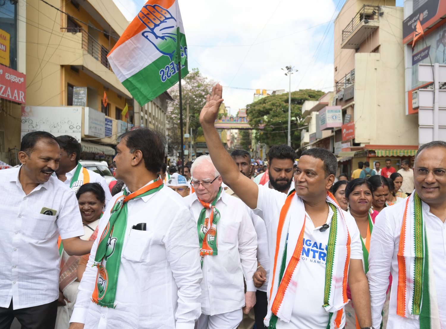 Mansoor Ali Khan walking through a Bengaluru neighbourhood with Congress workers, a party flag overhead.